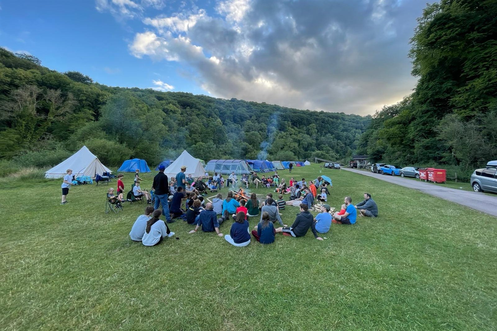 Group of men and children sitting on grass around a fire at a campsite